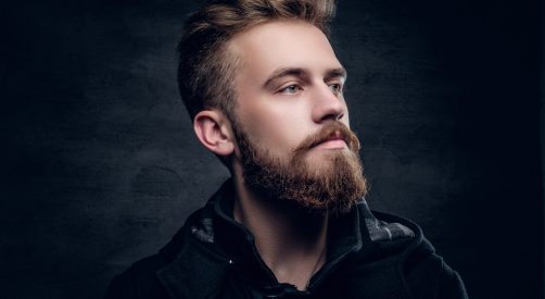 Portrait of bearded stylish young male. Portrait of a bearded urban male isolated with contrast illumination on grey vignette background.